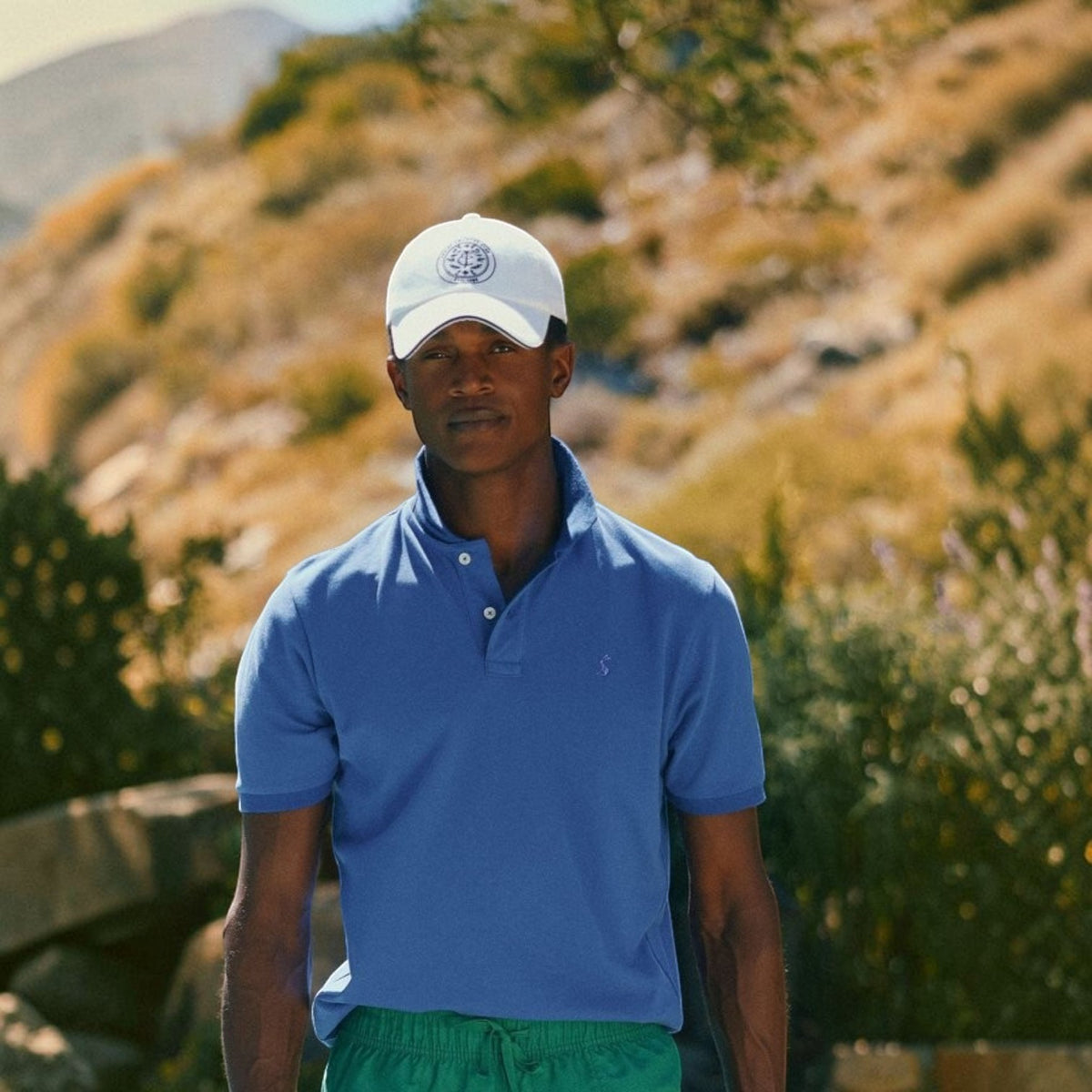 A man wearing a blue BATA LTD Joules Woody cotton pique polo shirt with an embroidered hare logo outdoors.