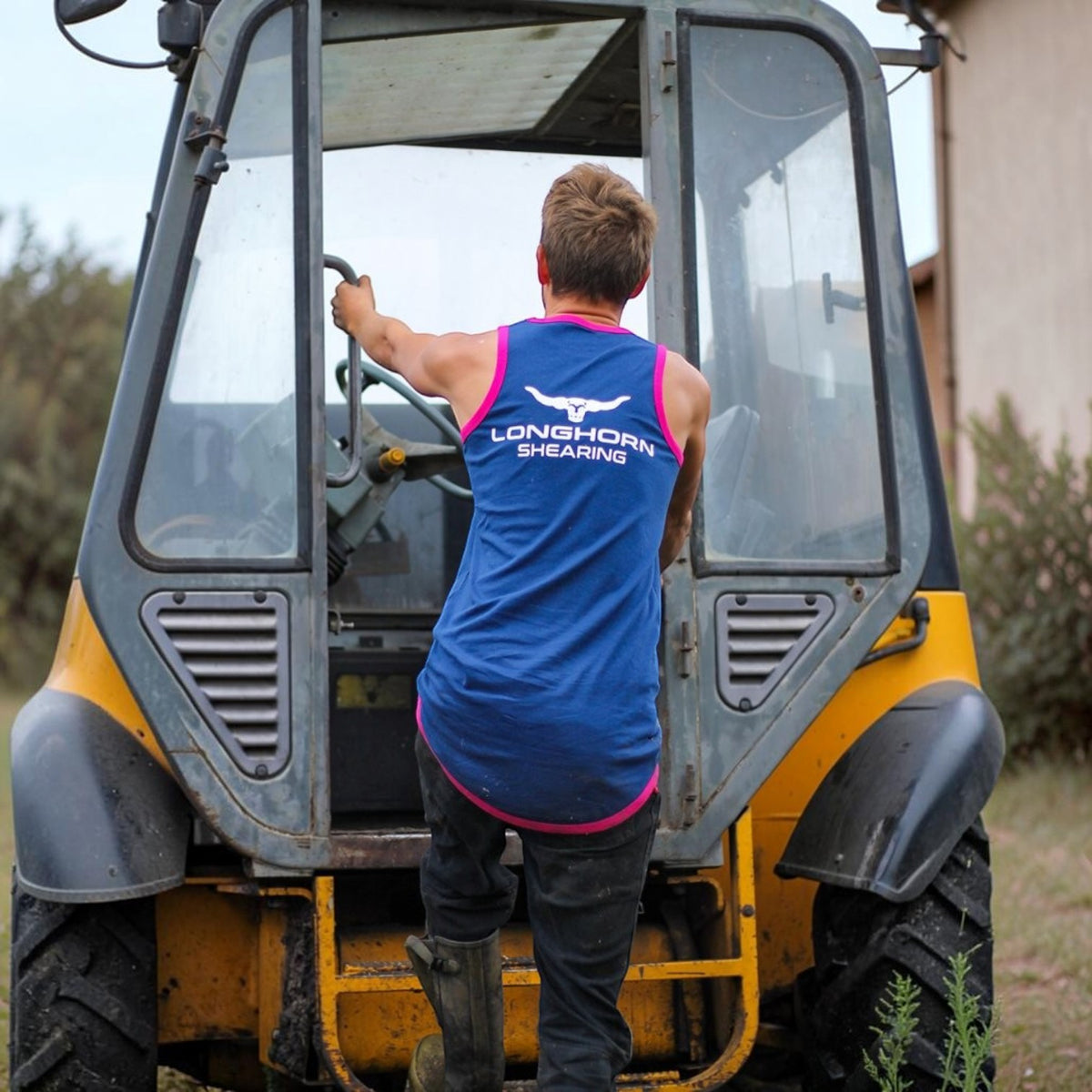 BATA LTD blue shearing singlet with pink contrast piping and long tail design worn by a man climbing into a tractor