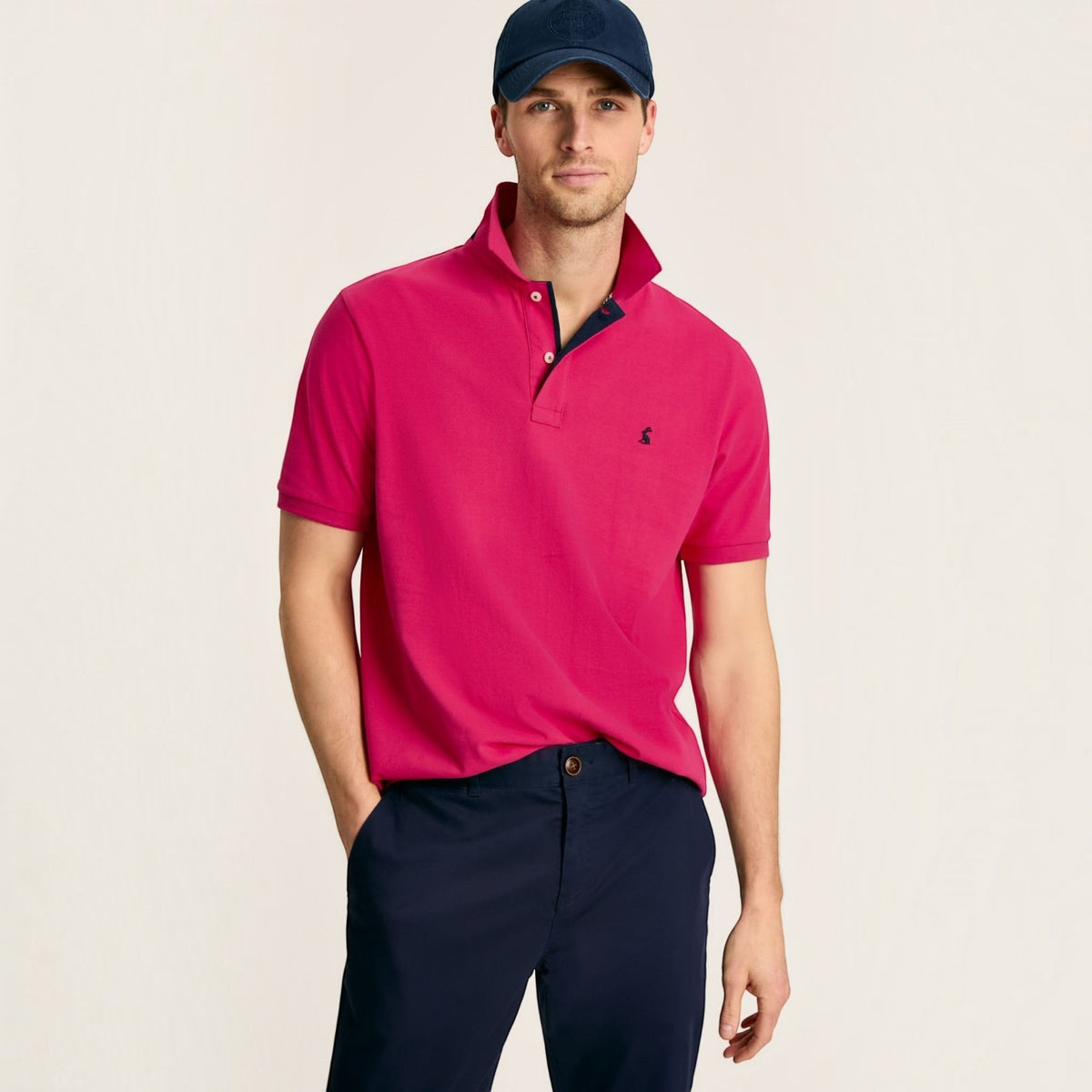 BATA LTD Joules pink cotton pique polo shirt with embroidered hare logo, worn by a man in a navy cap and trousers.
