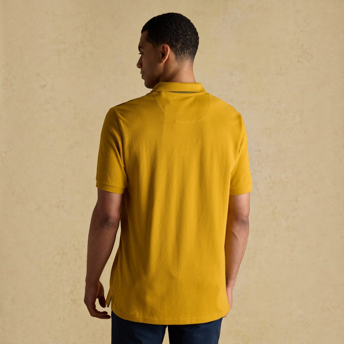 BATA LTD Joules Woody mustard yellow cotton pique polo shirt worn by a man, back view showing short sleeves.