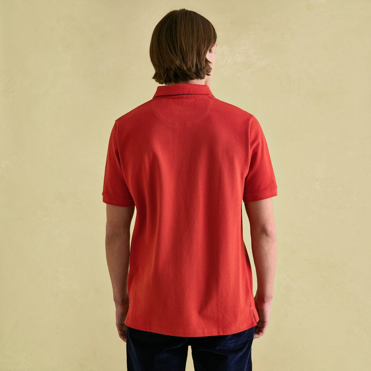 Back view of a man wearing a red BATA LTD Joules Woody cotton pique polo shirt with short sleeves.